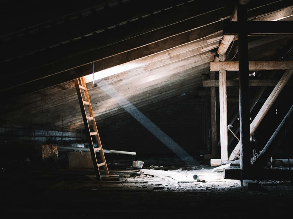 Light falling through a gap in the roof of a dark attic, with a wooden ladder against the rafters