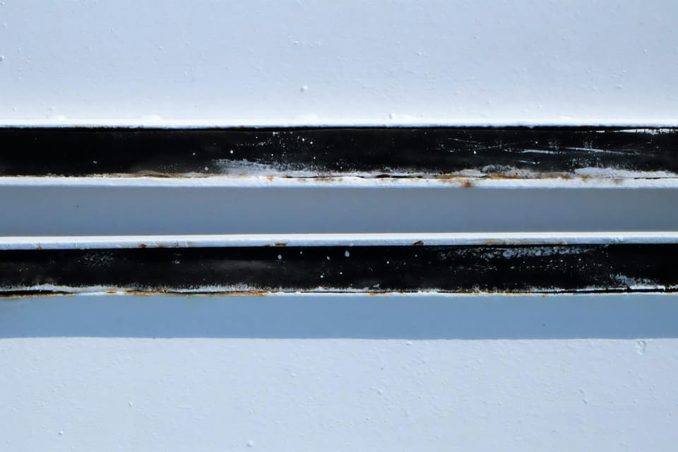 Close-up of white metal vent louvers with dark grime and specks of rust along the slats