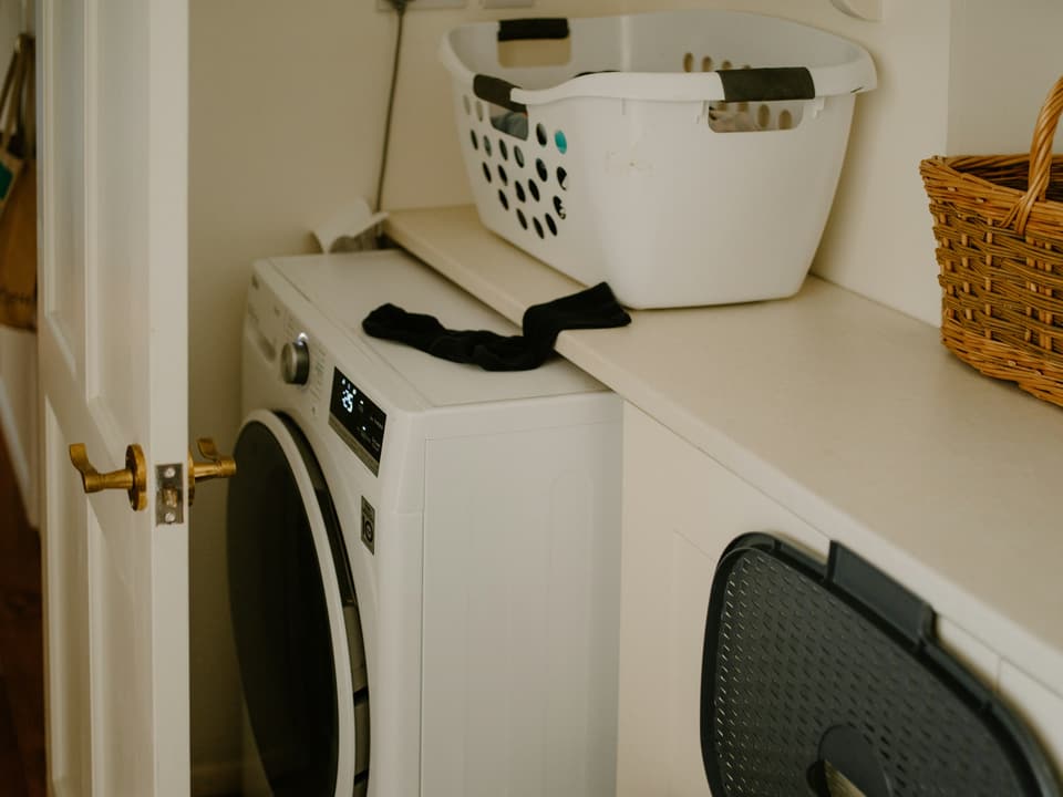A front-loading washing machine in a home laundry nook, with a laundry basket on the counter beside it